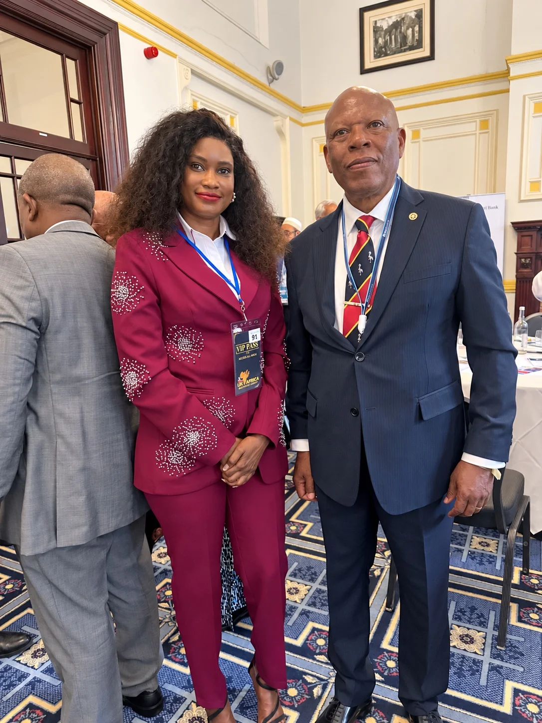 Doris Beth Atigo in a burgundy suit alongside another attendee in a navy suit at a summit gathering.